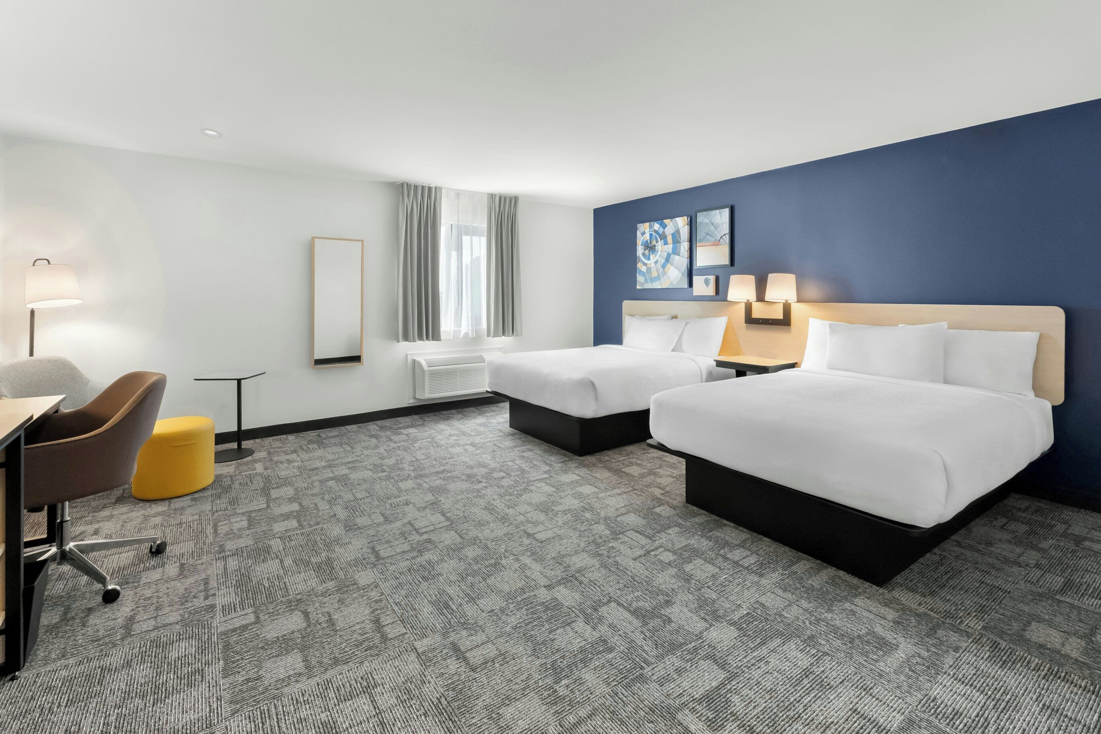 Une chambre d’hôtel avec deux lits, un bureau, une chaise et une fenêtre avec des rideaux.