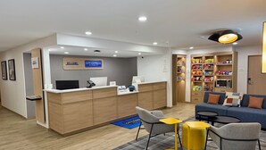 A hotel reception area with a wooden desk, a computer, a phone, and a seating area with a sofa and chairs.