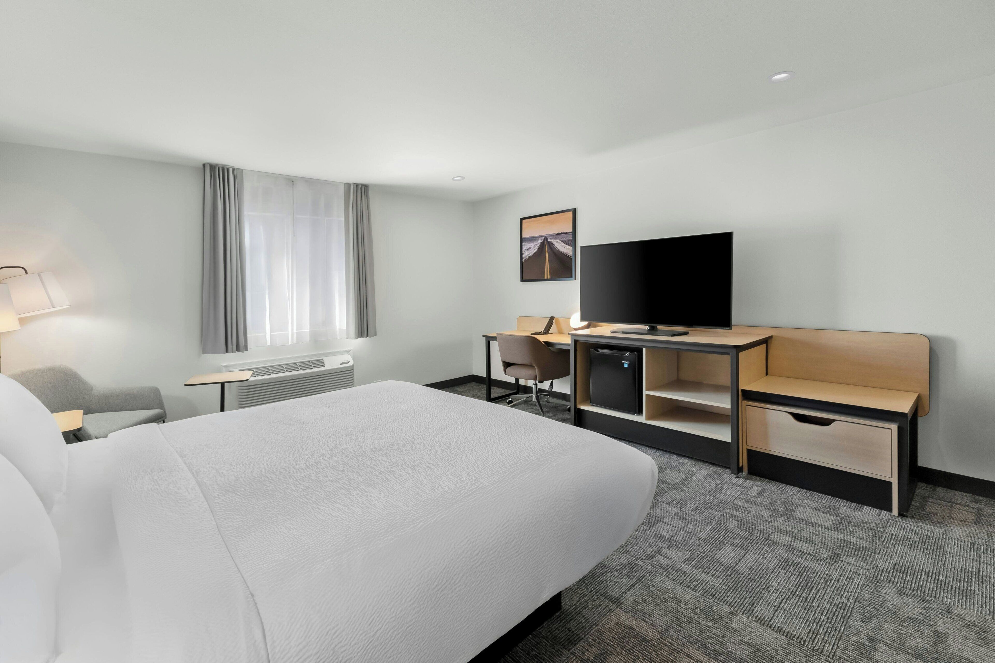 Habitación de hotel con cama, escritorio, silla, televisor y ventana con cortinas.