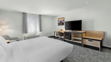 Habitación de hotel con cama, escritorio, silla, televisor y ventana con cortinas.
