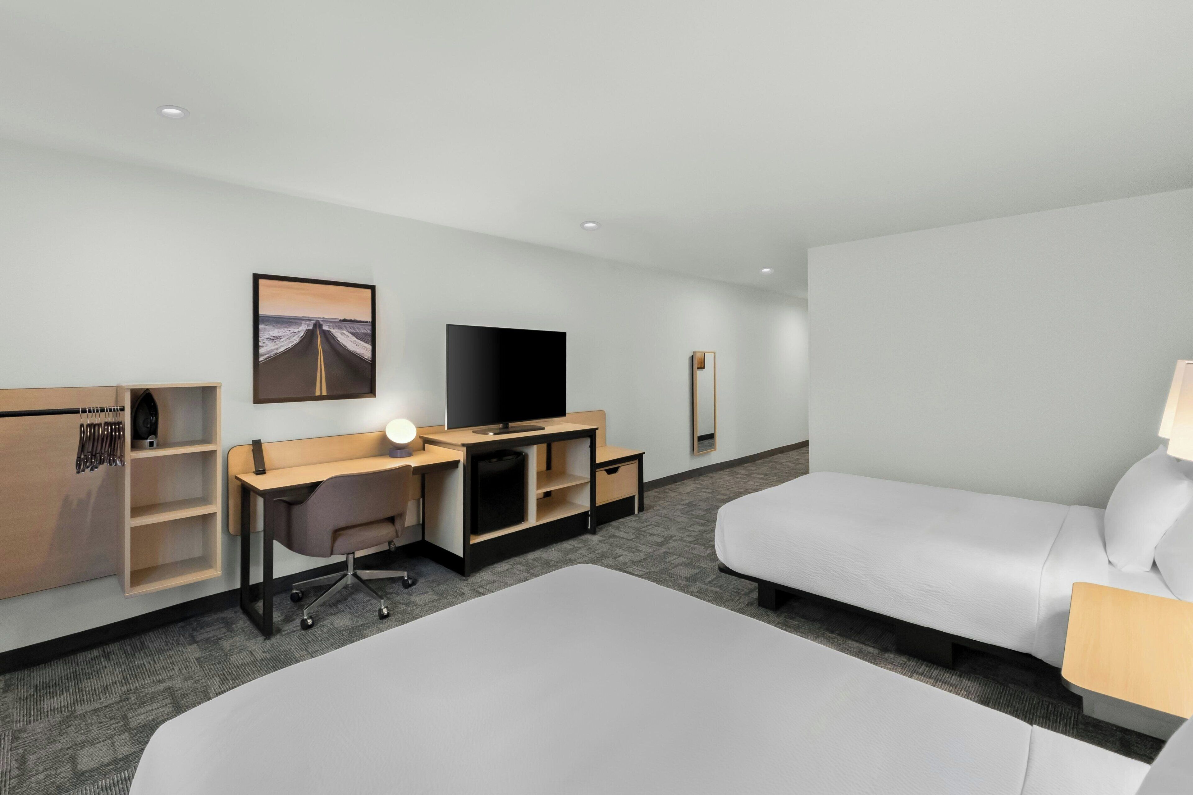 Una habitación de hotel con cama, escritorio, silla, televisión y un cuadro en la pared.