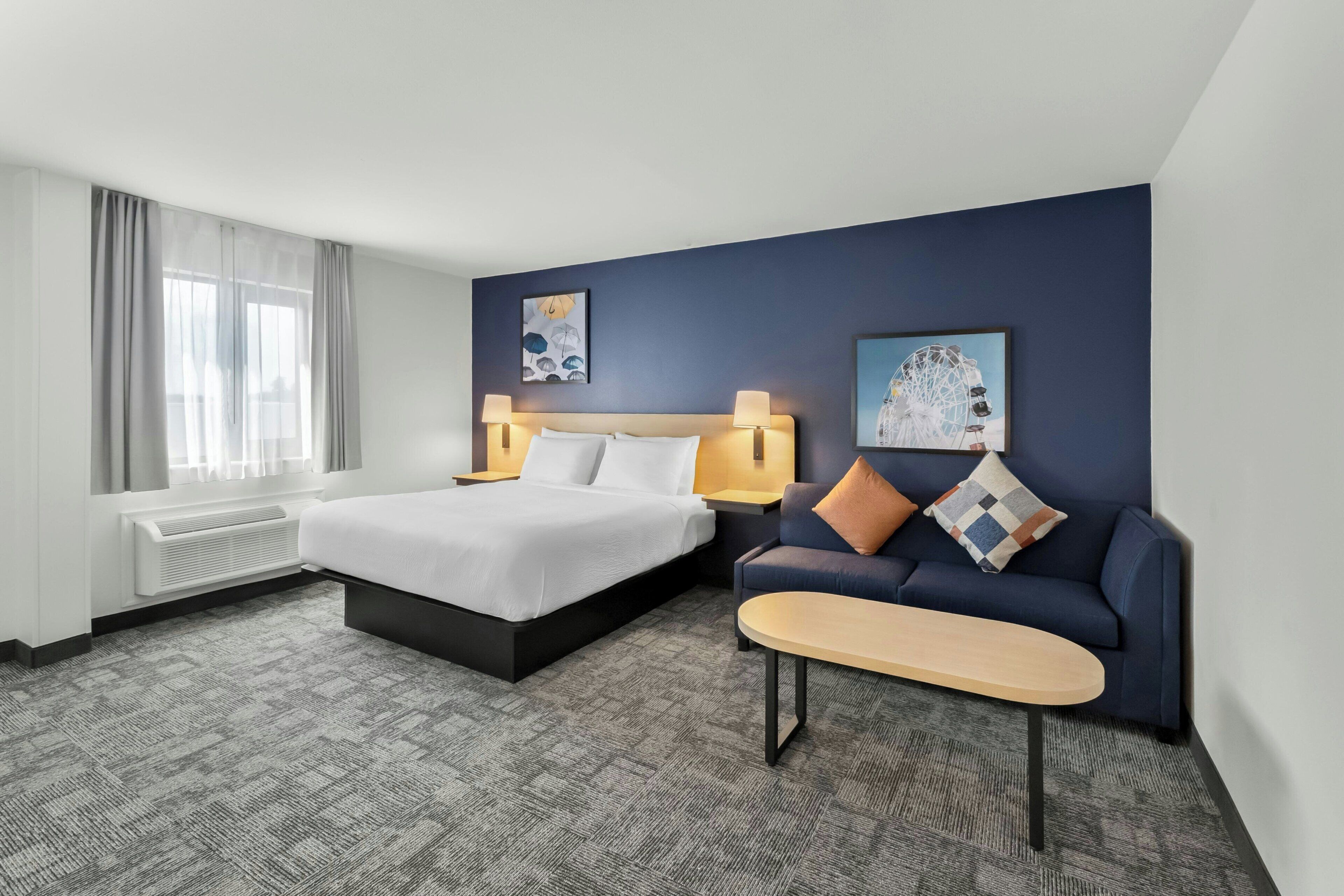 Une chambre d’hôtel avec un lit, un canapé, une petite table et deux lampes fixées au mur.