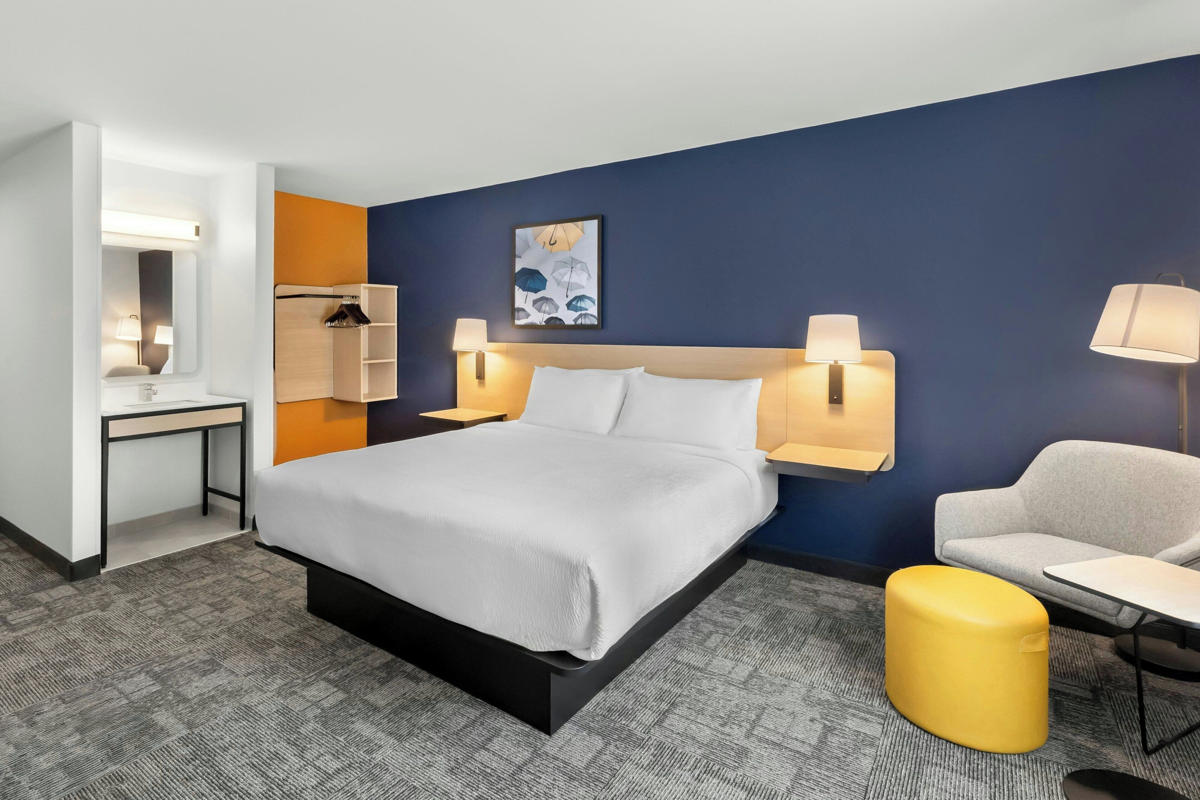 A hotel room with a large bed, bedside lamps, a desk, a chair, and a small table.