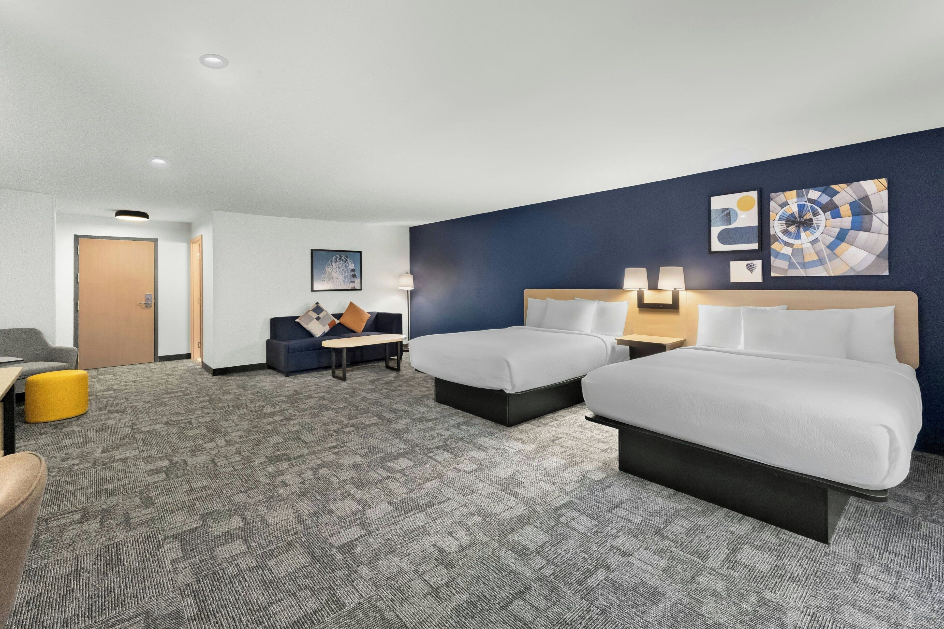 A hotel room with two beds, a sofa, a small table, and artwork on the walls.