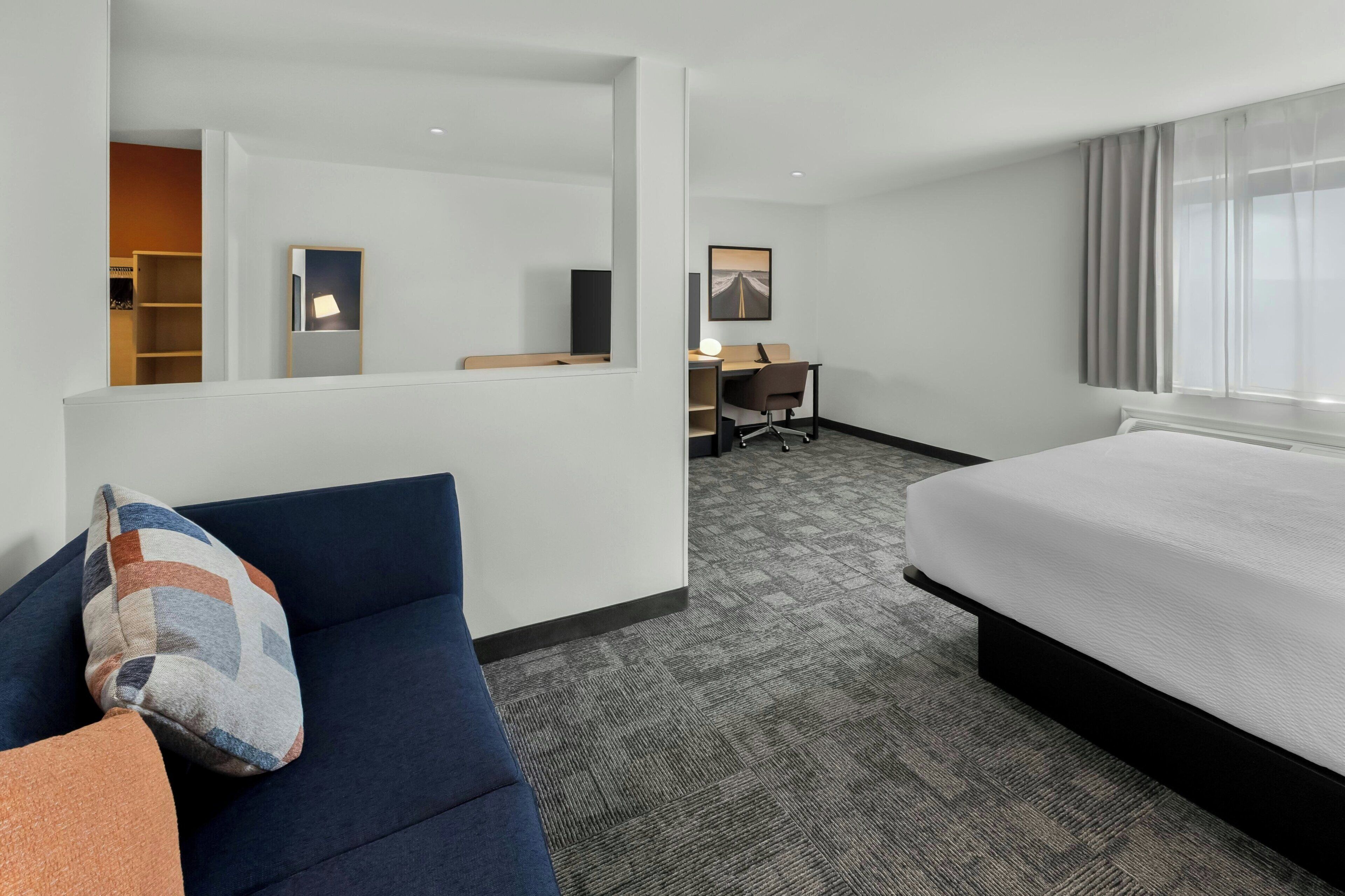 A hotel room with a bed, a desk, a chair, a sofa, and a large window.