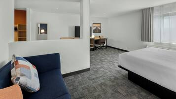 A hotel room with a bed, a desk, a chair, a sofa, and a large window.