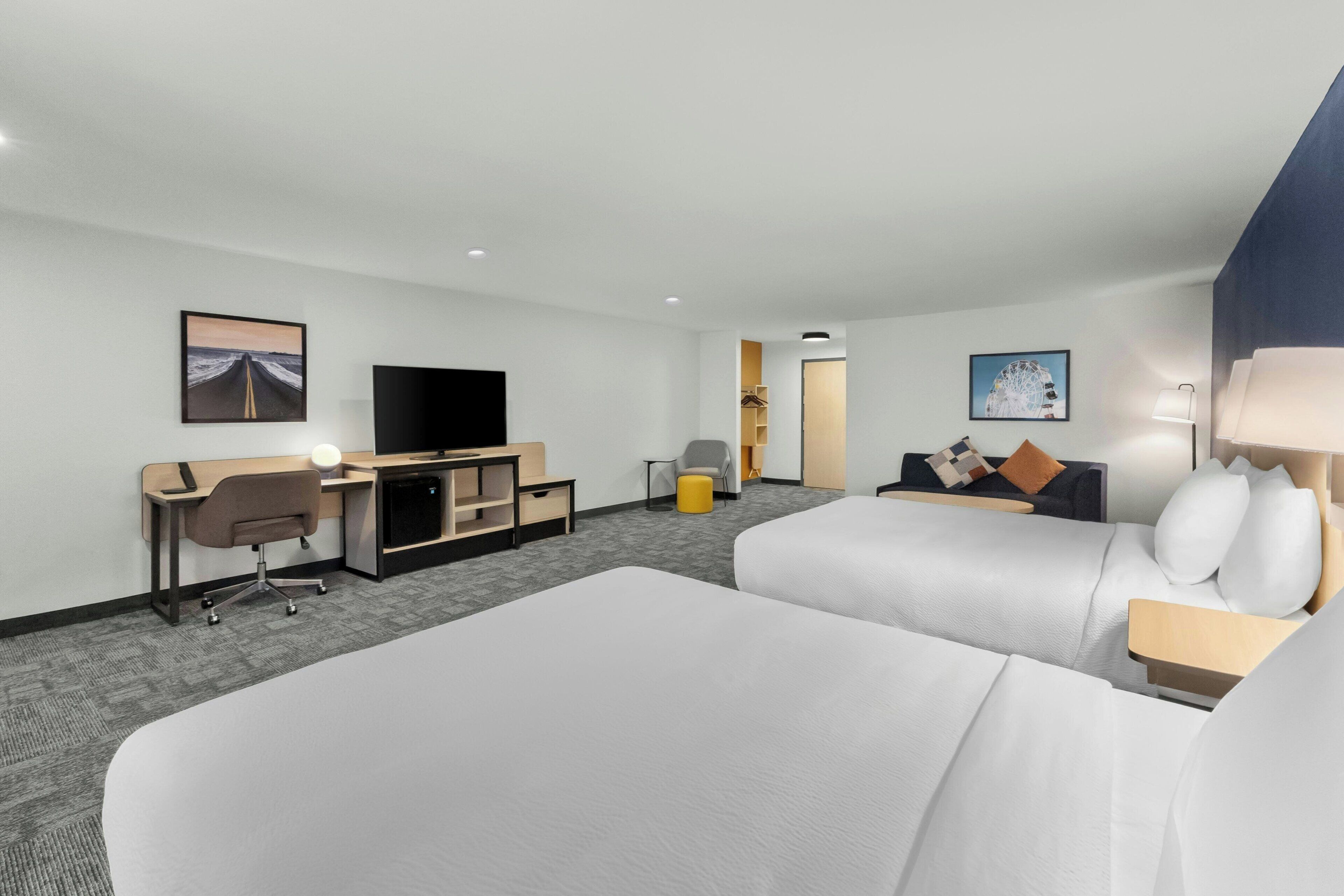A hotel room with a large bed, a desk with a chair, a television, and a small seating area with a sofa and pillows.