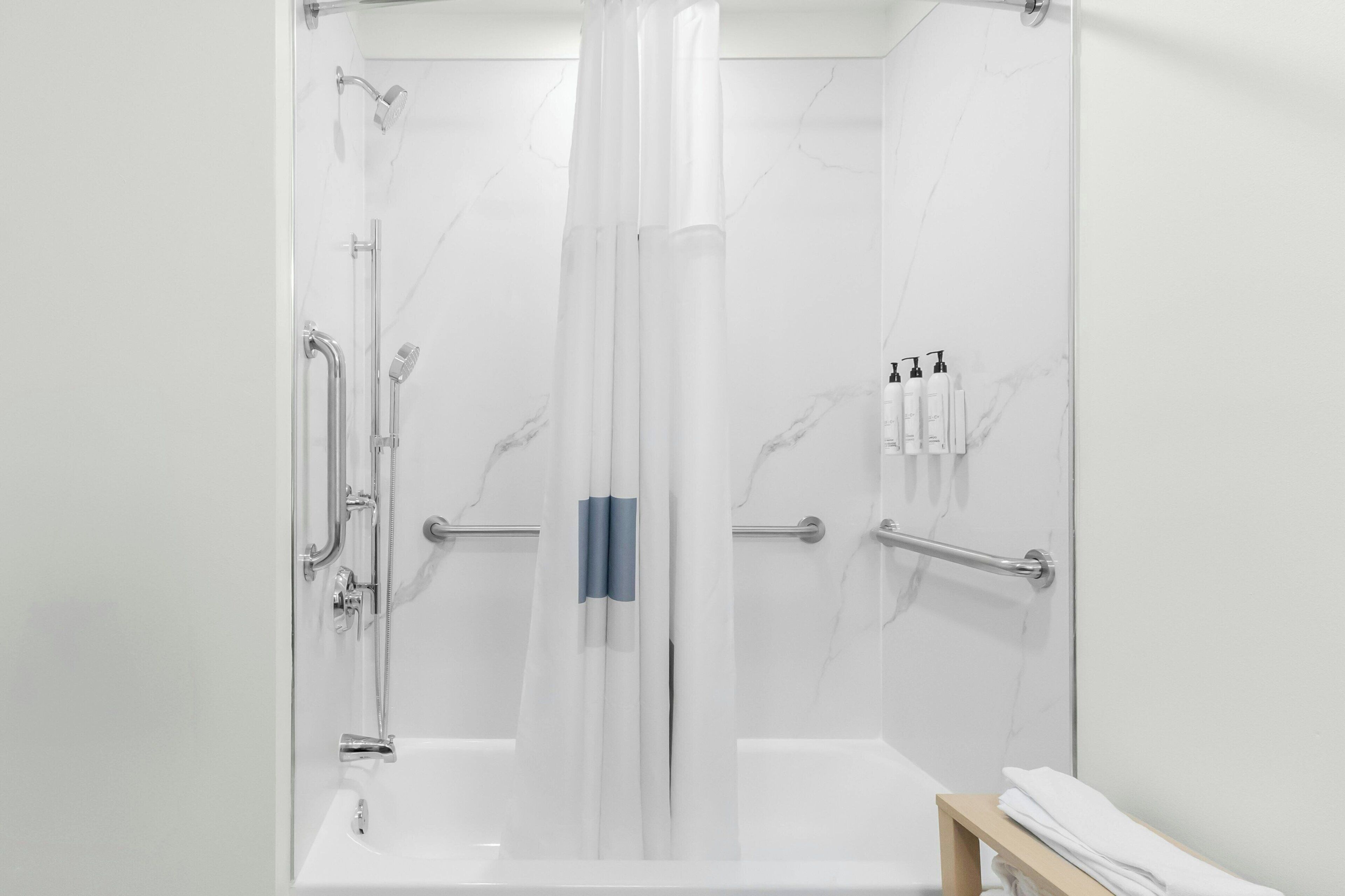 A modern bathroom with a glass-enclosed shower, a bathtub, and a handrail.