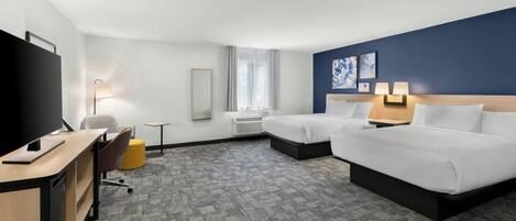 Habitación de hotel con dos camas, un escritorio con televisor, una silla, una mesita y una ventana con cortinas.