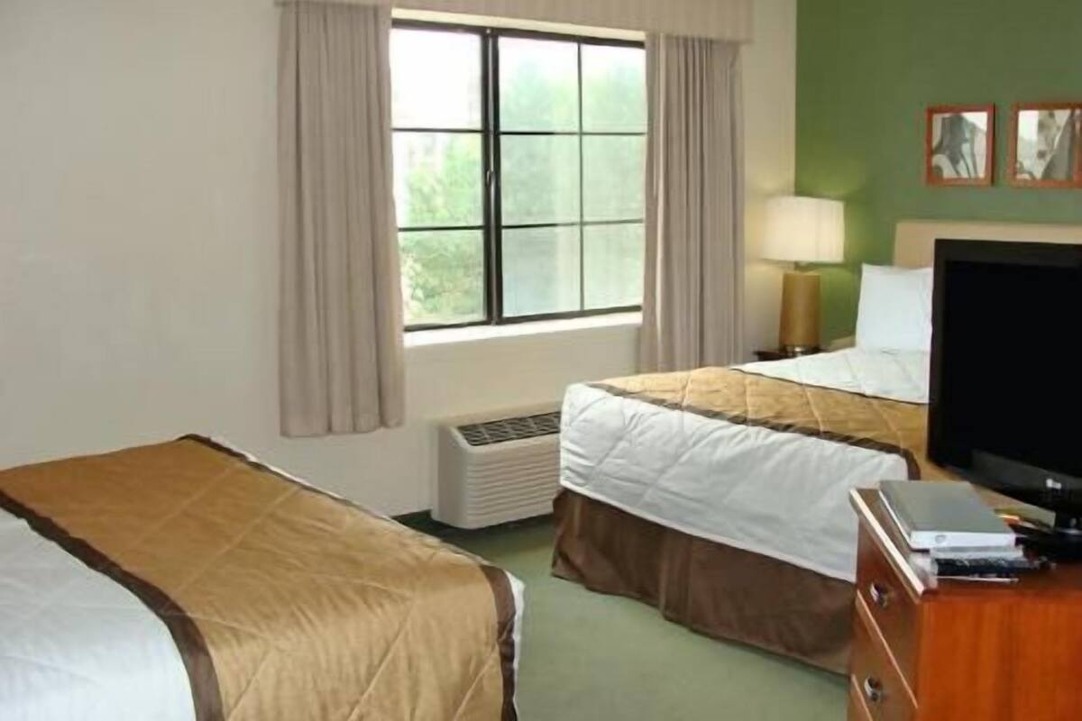 A hotel room with two beds, a window with curtains, a desk with a lamp, and a television.