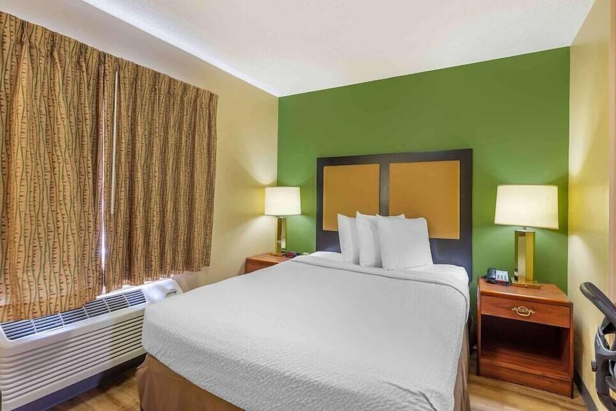 A hotel room with a bed, two bedside tables with lamps, a heater, and a curtain.
