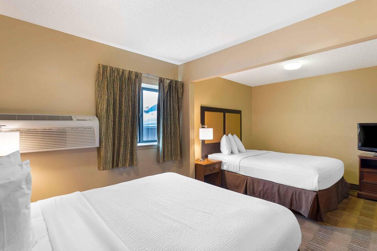 A hotel room with two beds, a TV, a lamp, and a window with curtains.