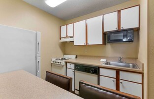 Cocina compacta con armarios blancos, microondas, estufa y lavavajillas.