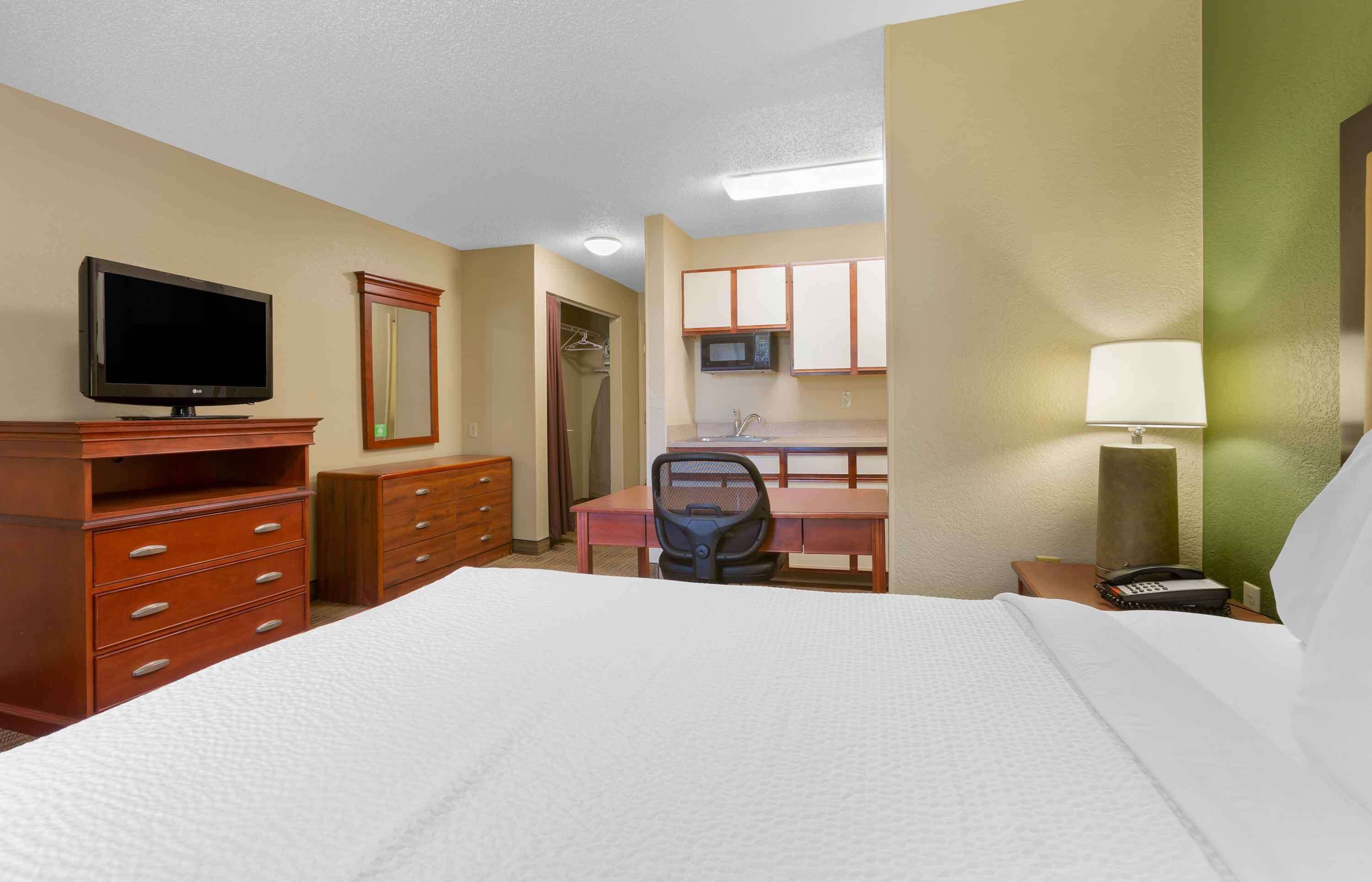A hotel room with a bed, a desk, a chair, a television, a microwave, and a telephone.
