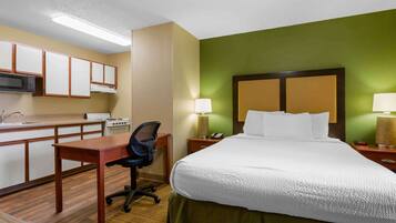 A hotel room with a bed, desk, microwave, and a small kitchenette.