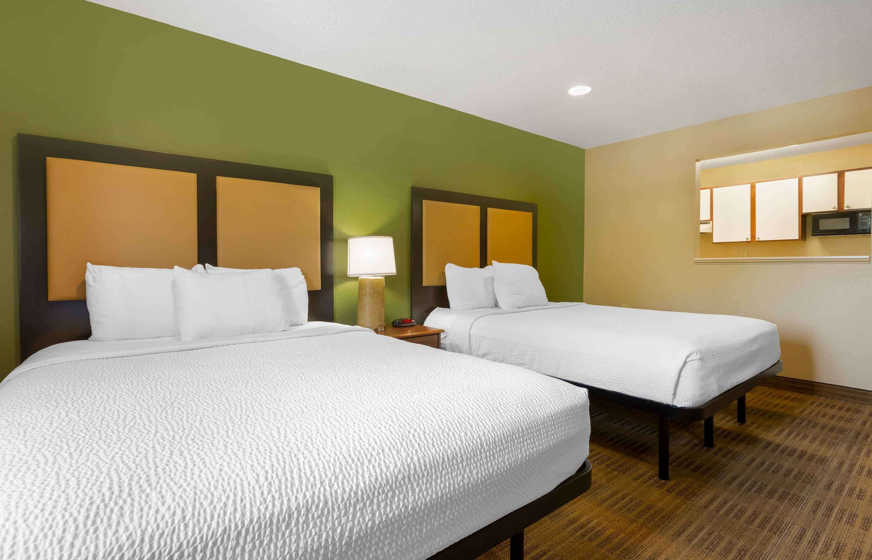 Habitación de hotel con dos camas, una mesita de noche, una lámpara y un microondas.