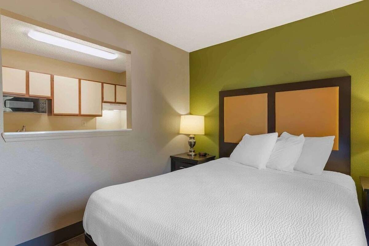 Una habitación de hotel con cama, mesita de noche, lámpara, microondas y armario.