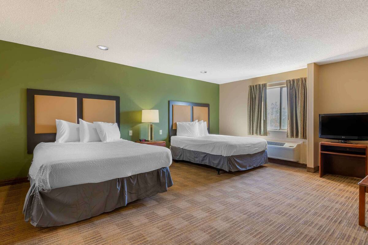 Habitación de hotel con dos camas, televisión y ventana con cortinas.