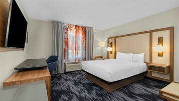 A hotel room with a bed, desk, chair, TV, and two bedside lamps.