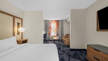 A hotel room with a large bed, a desk, a chair, and a TV.