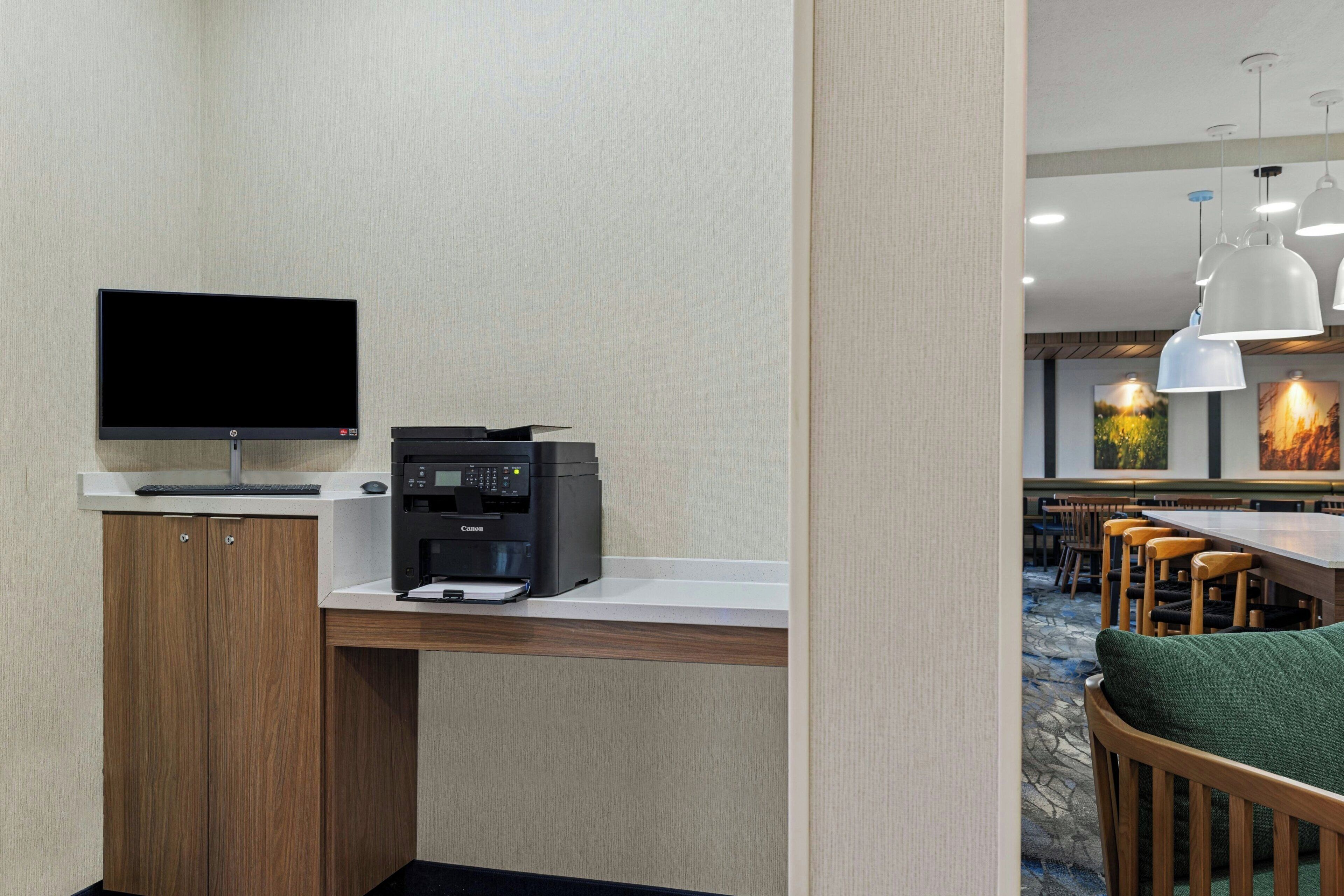 Habitación de hotel con escritorio, impresora y televisor. El comedor incluye sillas y mesas de madera.