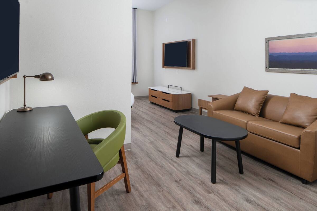 Un salon moderne avec une table noire, un fauteuil vert, un canapé en cuir marron et un téléviseur fixé au mur.