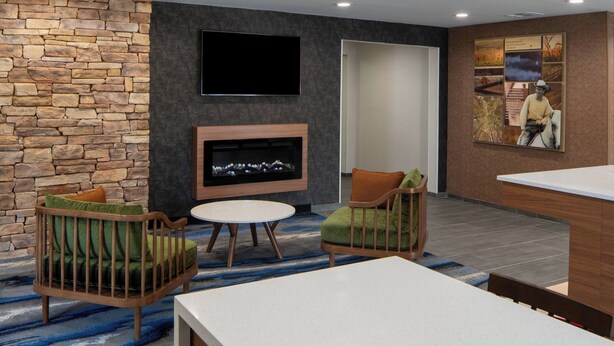 A modern living room with a stone wall, a flat-screen TV, a fireplace, and comfortable seating. - Fairfield Inn & Suites by Marriott Lake Charles Sulphur (Sulphur)
