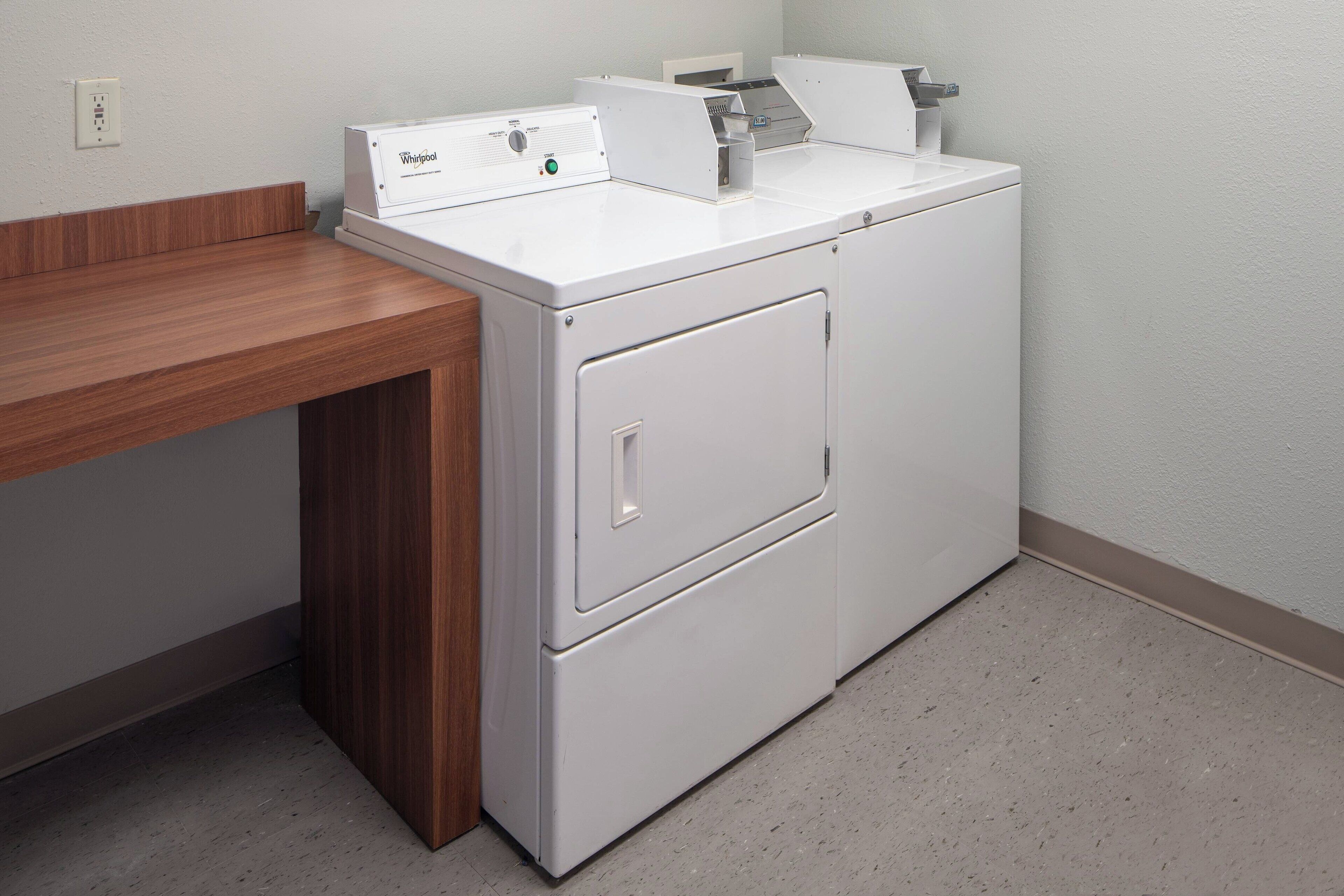 A compact, white front-loading washer and dryer unit with a wooden countertop on the left.