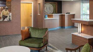 A hotel lobby with a reception desk, a green armchair, a brown armchair, and a round table. - Fairfield Inn & Suites by Marriott Lake Charles Sulphur (Sulphur)