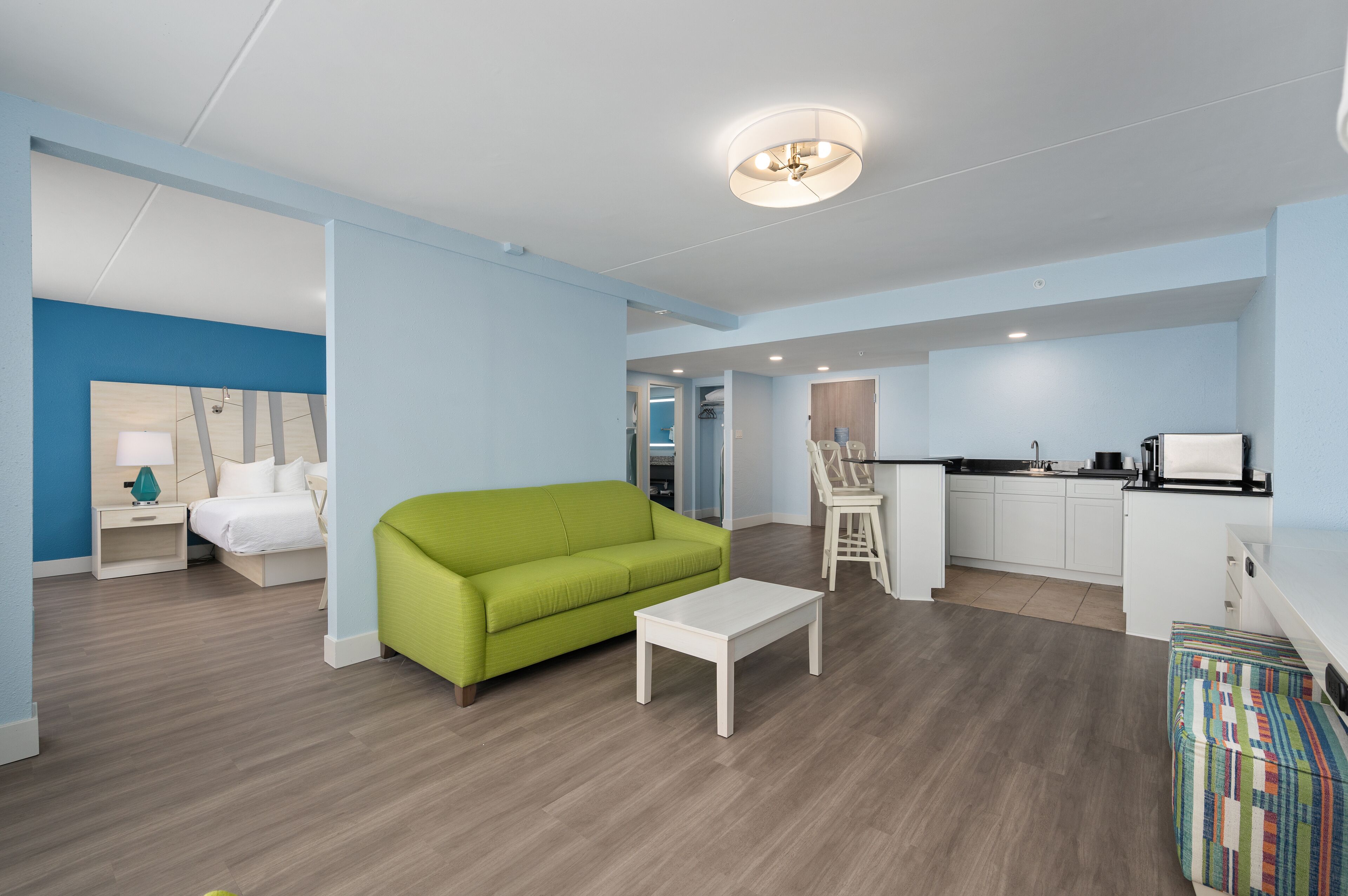 Una sala de estar moderna con un sofá verde, una mesa de centro blanca y una cocina con armarios blancos y una encimera negra.