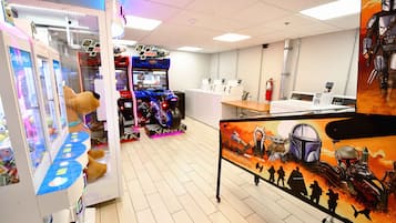 Experience the excitement of gaming with a variety of machines, including claw games and racing simulators, set against a vibrant Star Wars mural.