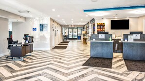 A hotel reception area with a herringbone patterned floor, reception desks, a flat-screen TV, and a view of the lobby. - Fenwick Inn (Ocean City)