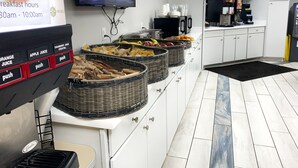 A buffet area with a self-serve juice dispenser, baskets of fruits, and a kitchen in the background.