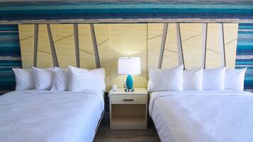 Habitación de hotel con dos camas, una mesita de noche con lámpara y una pared con diseño azul y amarillo.