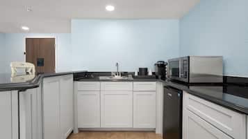 Cozinha compacta com armários brancos, bancada preta, micro-ondas e cafeteira.