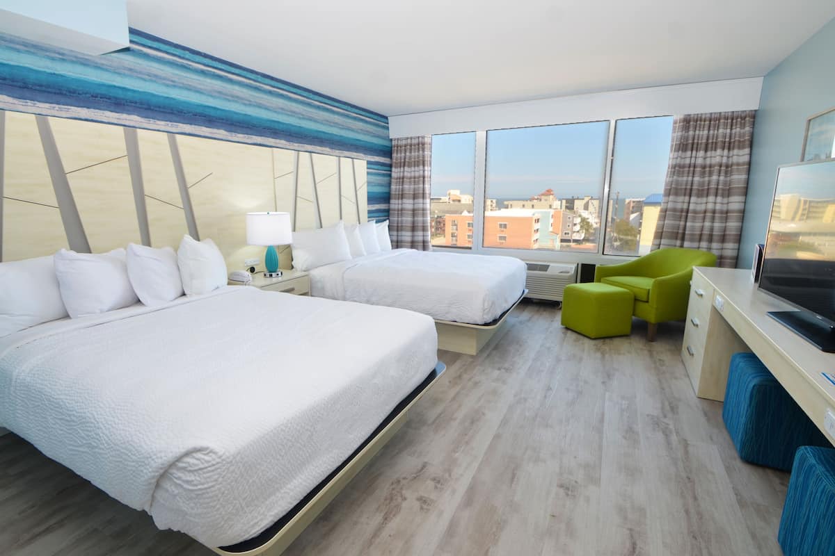 A hotel room with two beds, a desk, a chair, and a large window offering a city view.