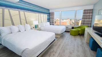 Een hotelkamer met twee bedden, een bureau, een stoel en een groot raam met uitzicht op de stad.