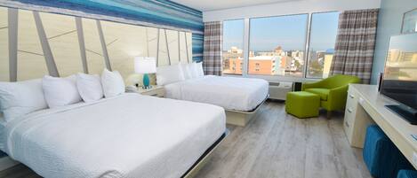 A hotel room with two beds, a desk, a chair, and a large window offering a city view.