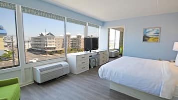 Ein modernes Hotelzimmer mit einem großen Bett, einem Schreibtisch mit Computer, einem Fernseher und Blick auf die Stadt durch große Fenster.