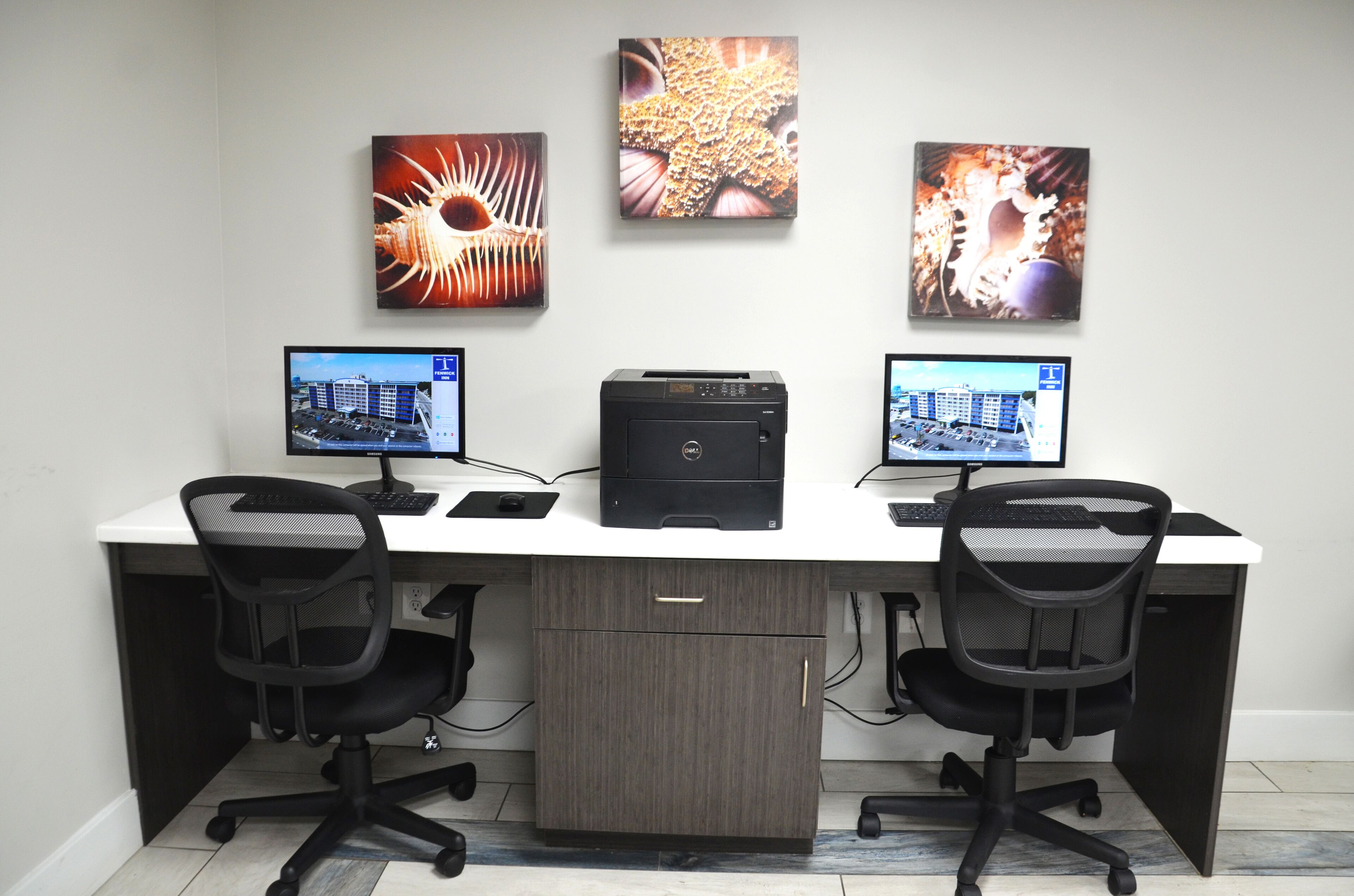 A modern office desk with two monitors, a printer, and two office chairs.