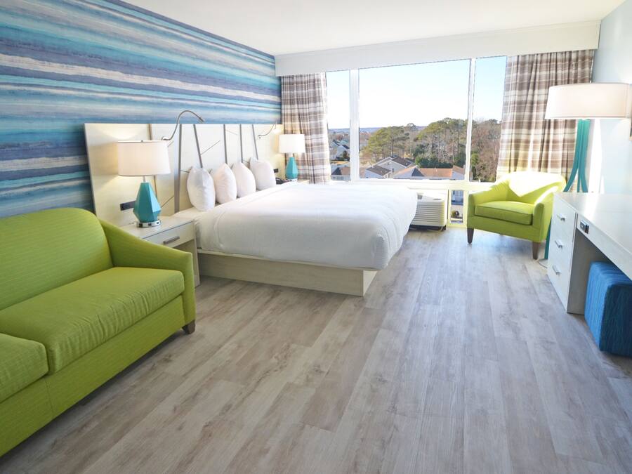 A hotel room with a large bed, a green sofa, a desk with a TV, and a view of the outside.