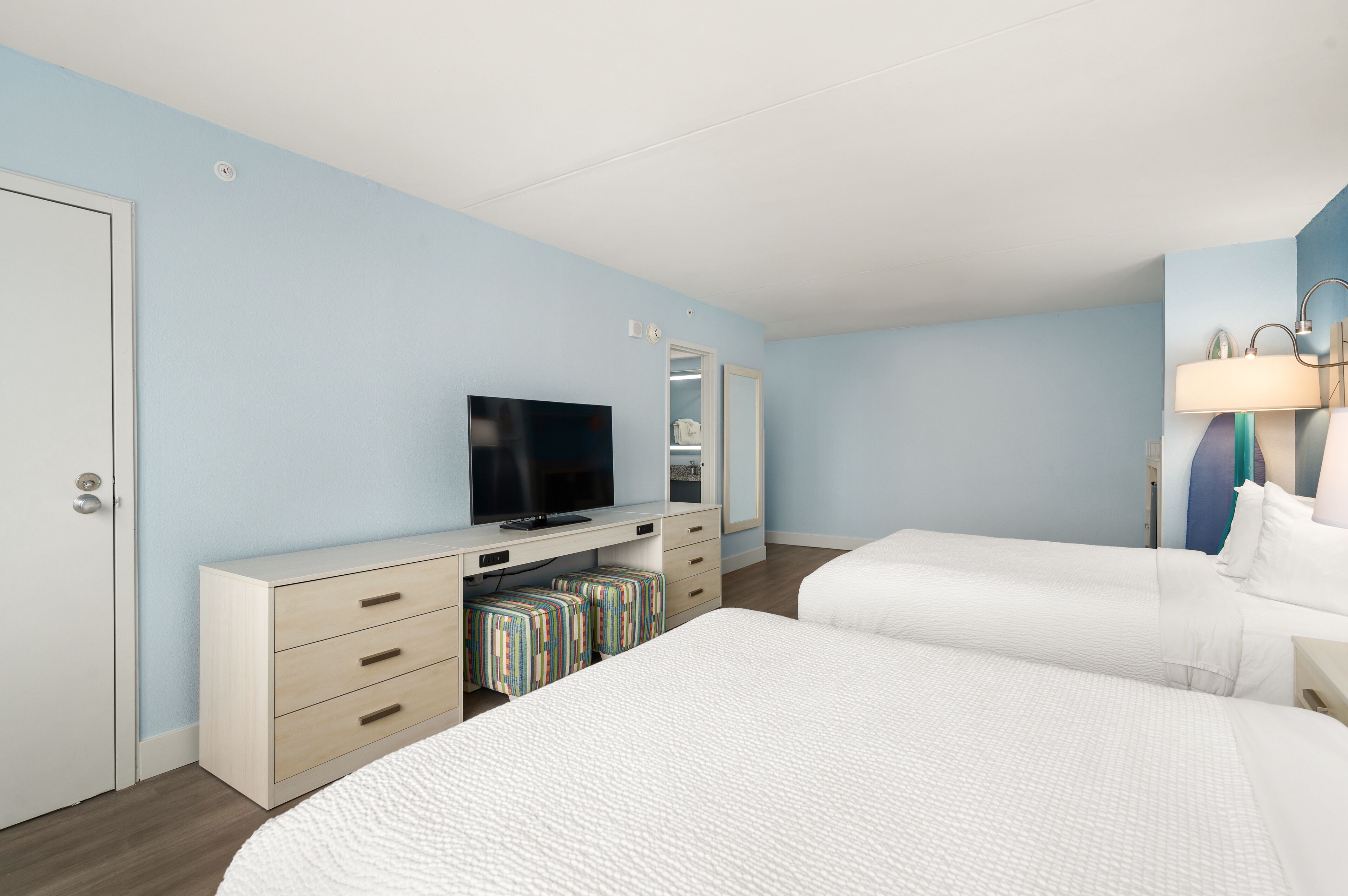 A hotel room with a bed, a TV, a dresser, and a mirror.