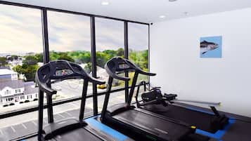 A gym with two treadmills and a rowing machine, large windows with a view of a residential area.