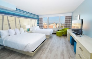 A hotel room with two beds, a desk with a TV, and a view of the city through large windows.