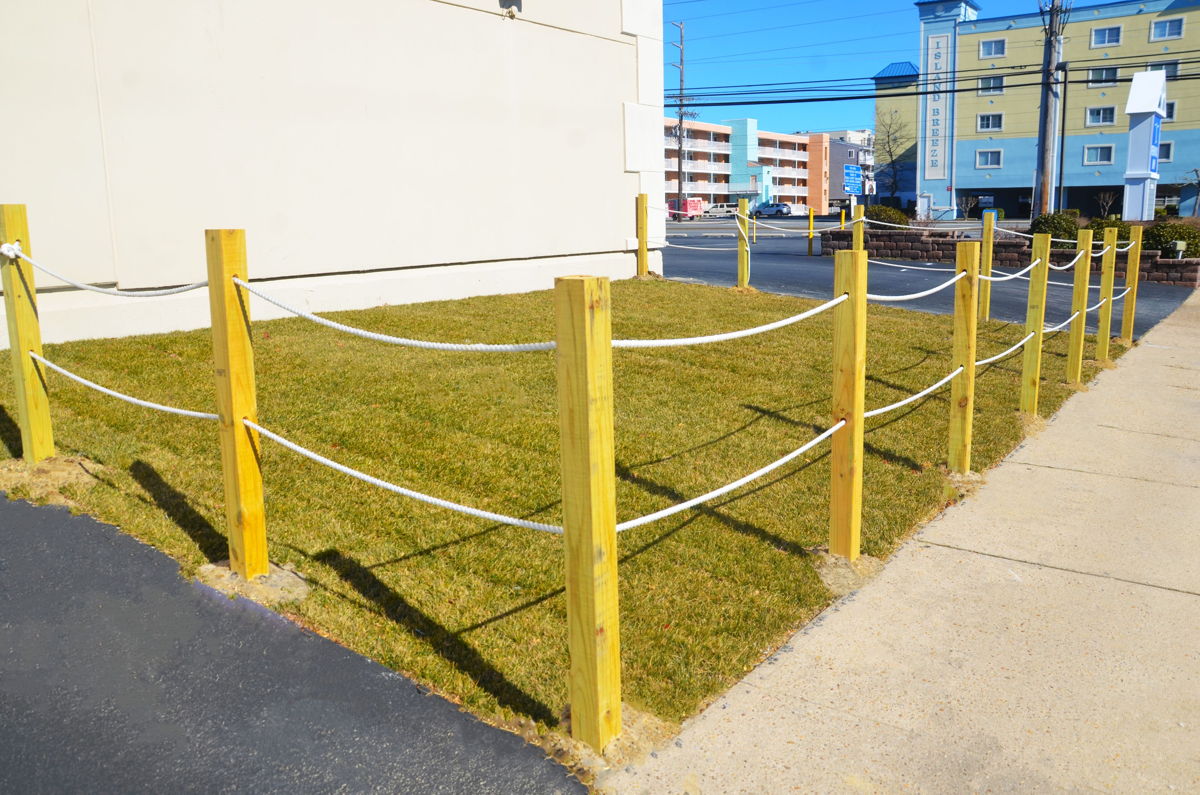 Zona verde con una barrera de cuerda y una acera al lado de un edificio.