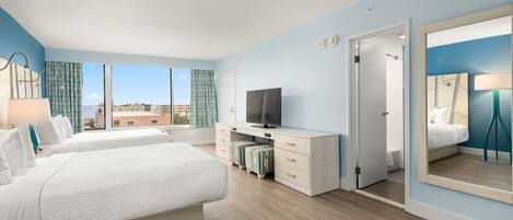 Habitación de hotel con una cama grande, televisión, escritorio con computadora, espejo y vista panorámica de la ciudad.