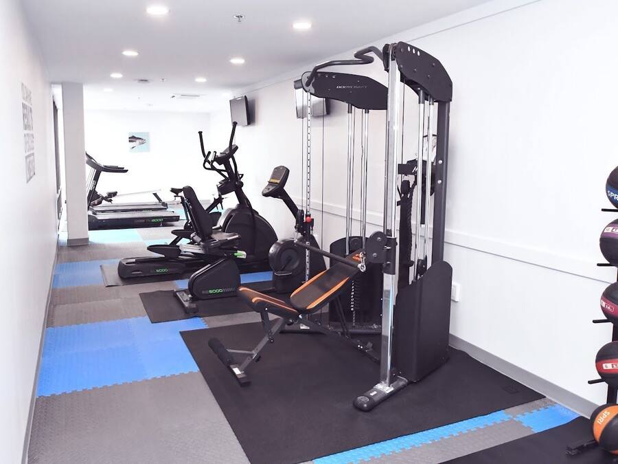 A gym with exercise equipment, a wall-mounted rack of balls, and a blue and gray floor.