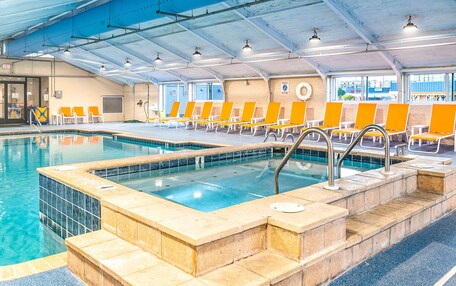 An indoor swimming pool with clear water, tiled steps, and orange lounge chairs.