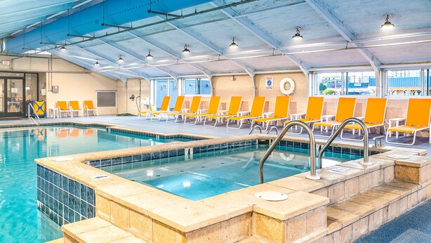 An indoor swimming pool with clear water, tiled steps, and orange lounge chairs. - Fenwick Inn (Ocean City)