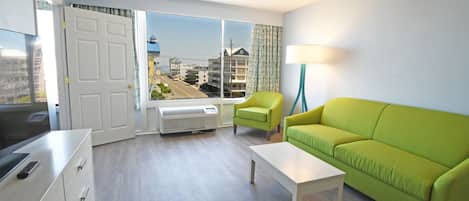 A modern living room with a green sofa, a white coffee table, and a bright window with a view of buildings.